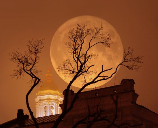 Supermoon with a church and a tree in foggy weather